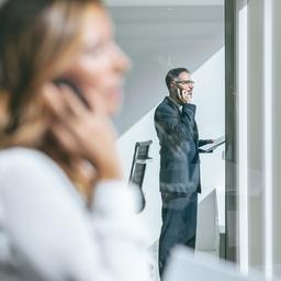 Eine Frau und ein Mann telefonieren mit ihren Smartphones in einem Büro.
