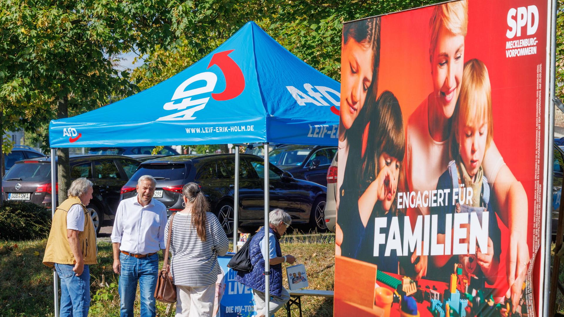 In Schwerin ist neben einem Informationsstand der AfD ein SPD-Wahlkampfplakat zu sehen. | Jens Büttner/dpa