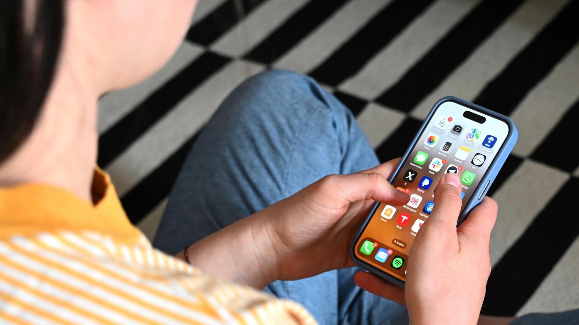 Eine Jugendliche sitzt auf dem Boden und nutzt ein Smartphone | dpa