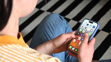 Eine Jugendliche sitzt auf dem Boden und nutzt ein Smartphone