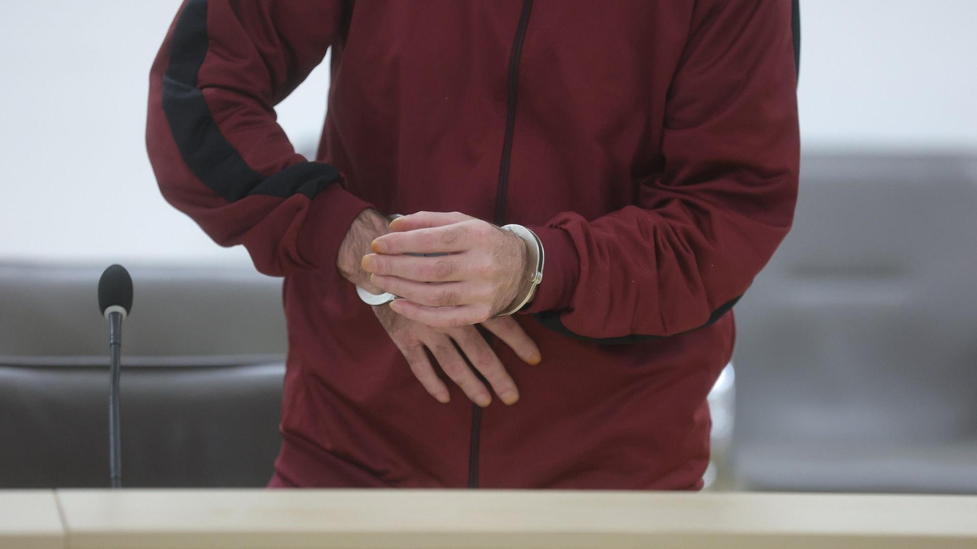 Der Angeklagte steht mit Handschellen im Gerichtssaal. | picture alliance/dpa | Bodo Schackow
