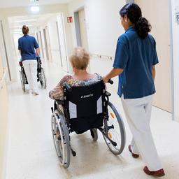 Zwei Pflegerinnen schieben Patientinnen in Rollstühlen über den Flur einer Pflegeeinrichtung.