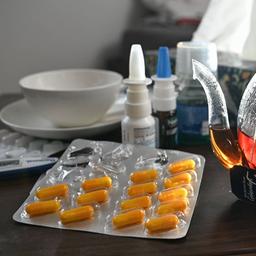 Medikamente und eine Kanne und Tasse Tee zur Bekämpfung einer Erkältung sind auf einem Nachttisch aufgestellt. 