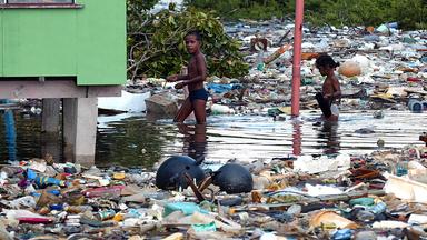 Kinder auf einem Pazifik-Atoll waten durch Müll und Wasser.