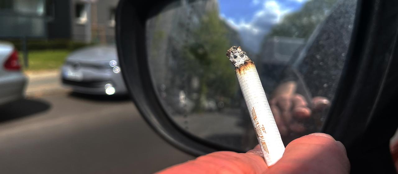 Ein Autofahrer hält eine brennende Zigarette aus dem Fenster.