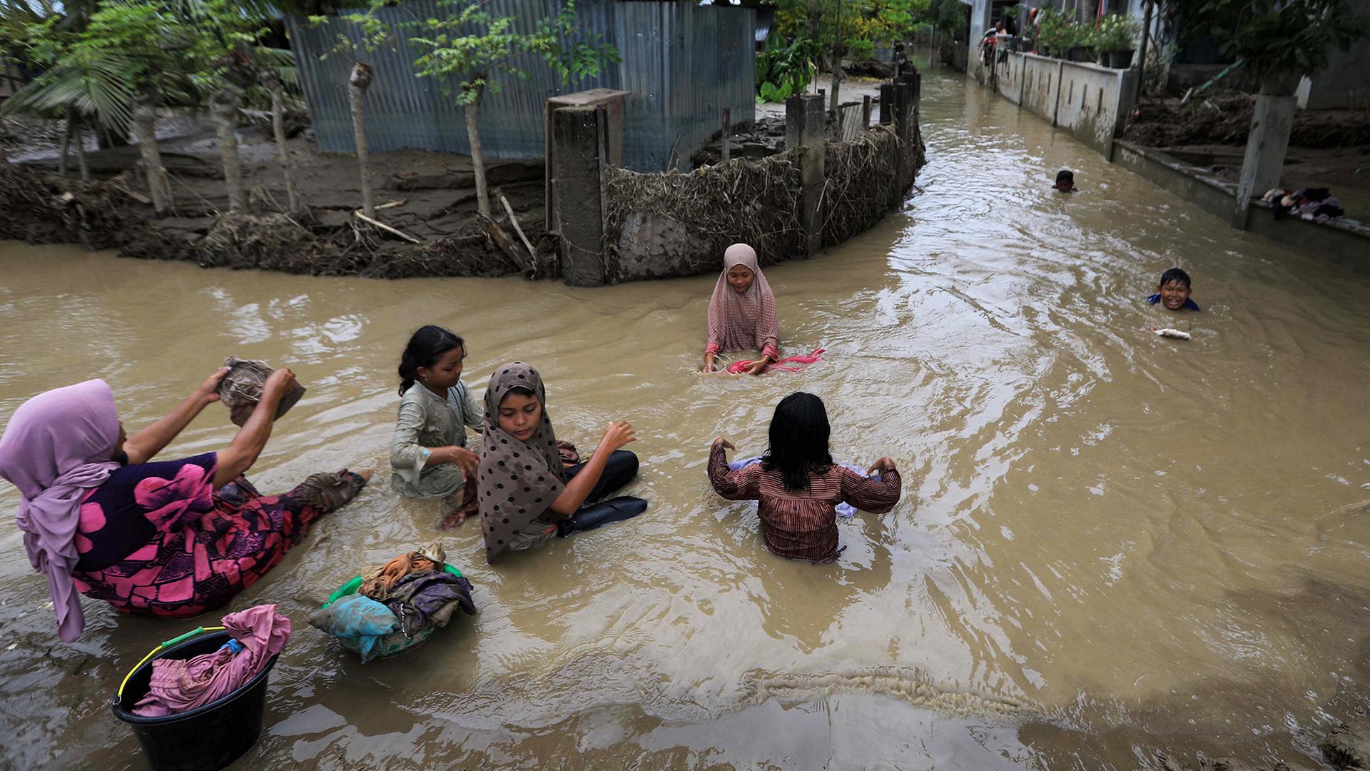 Menschen waschen Wäsche auf einer überfluteten Straße. | EPA