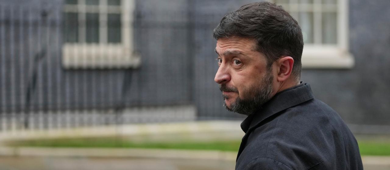 Wolodymyr Selenskyj schaut mit skeptischem Blick über seine Schulter.