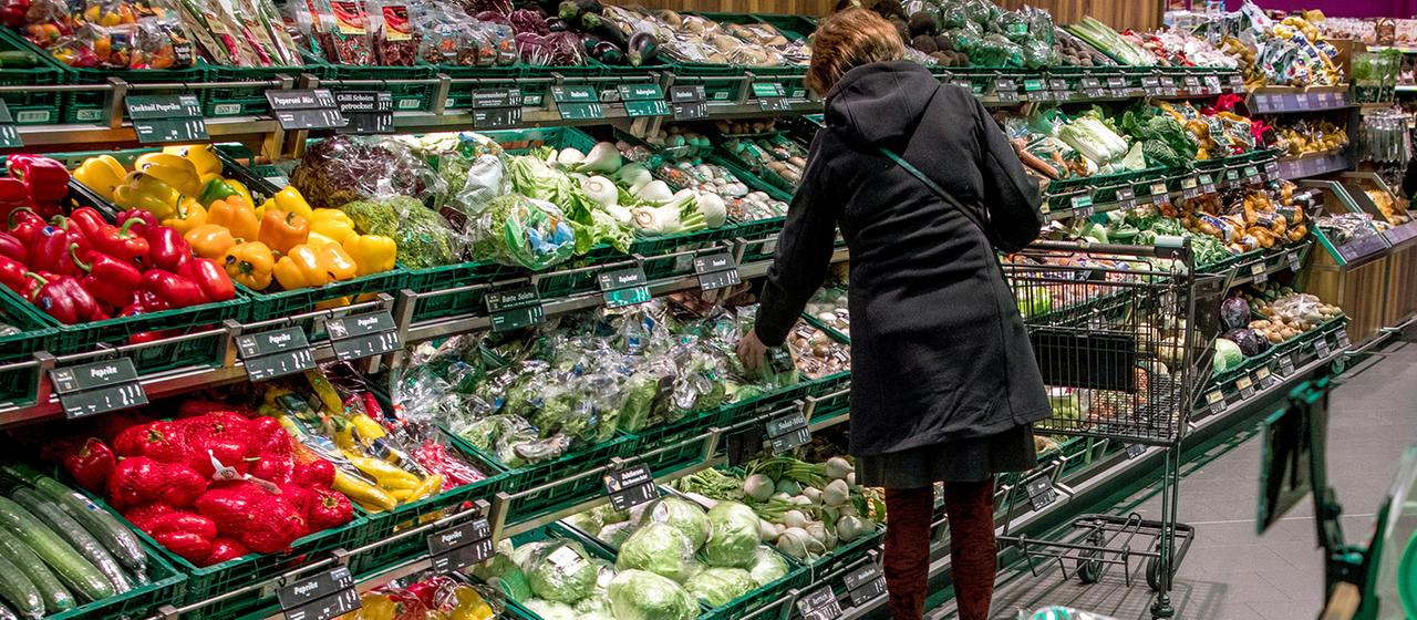 Eine Frau steht an einem Gemüseregal eines Supermarktes.