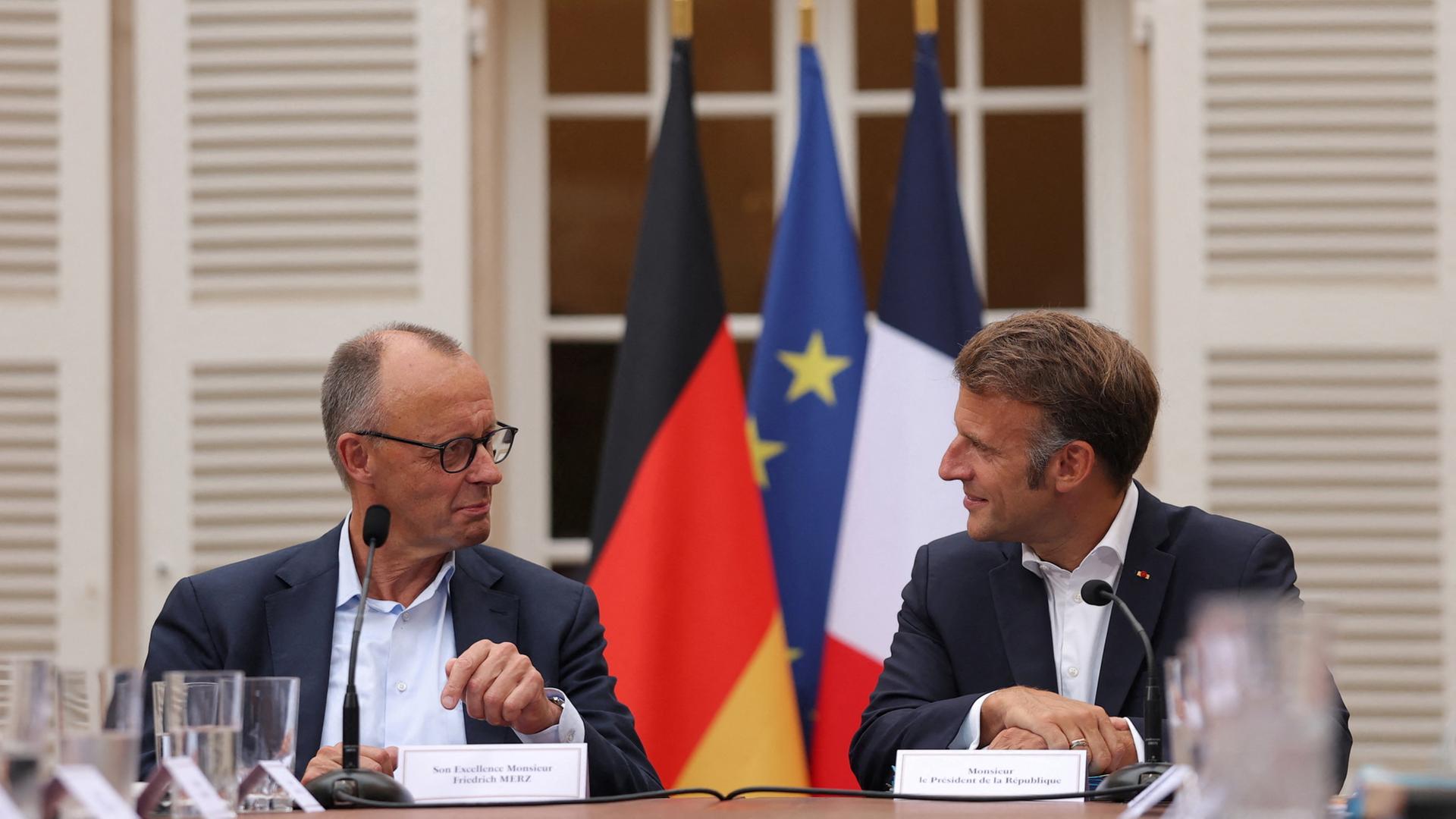 Friedrich Merz und Emmanuel Macron sitzen nebeneinander und schauen sich an. | EPA