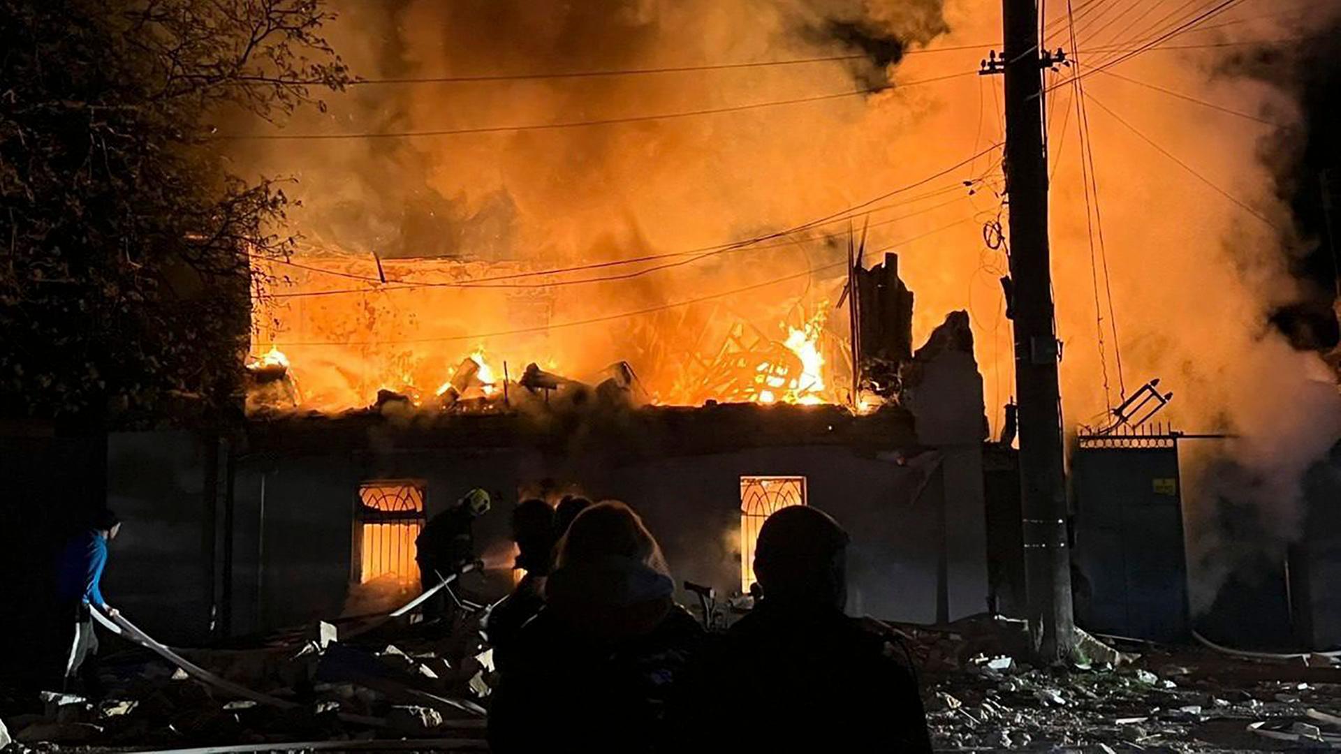 Menschen stehen vor einem zerstörten, brennenden Haus. | EPA