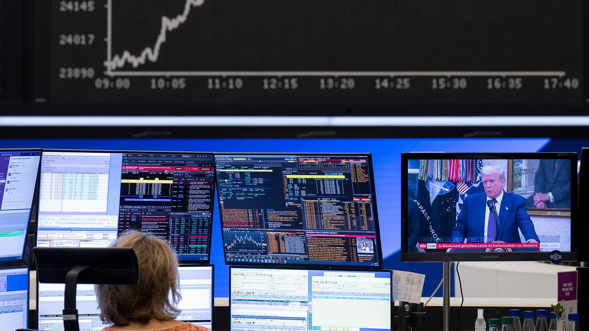 Eine Händlerin an der Börse Frankfurt sitzt vor Bildschirmen. Auf einem davon ist Donald Trump zu sehen. | picture alliance/dpa