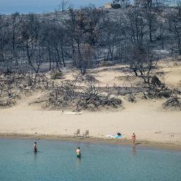 Menschen baden auf der griechischen Insel Rhodos an einem von Waldbränden betroffenen Strand.