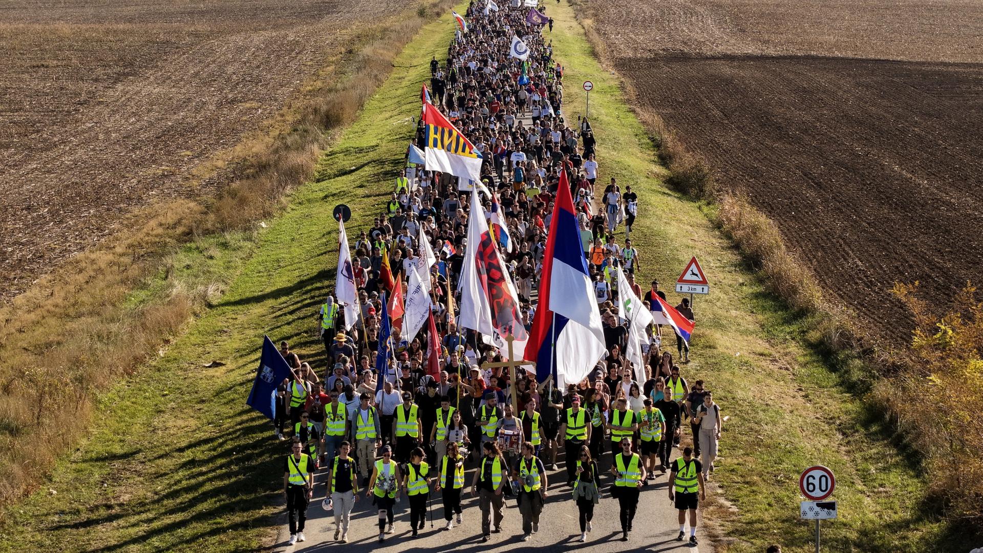 Ein Zug von Demonstrierenden läuft mit Flaggen an Feldern vorbei | AP