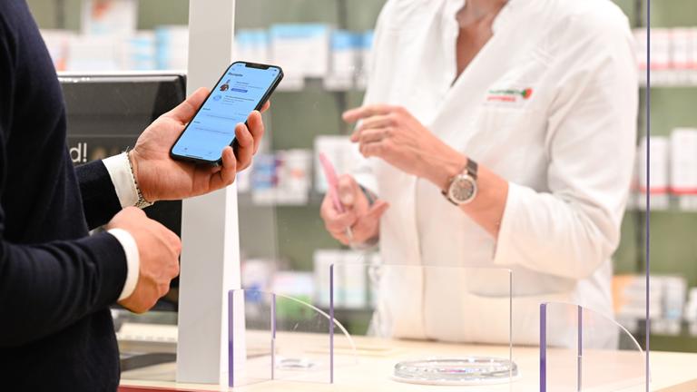 Ein Mann hält in einer Apotheke das Handy mit einem E-Rezept in der Hand.