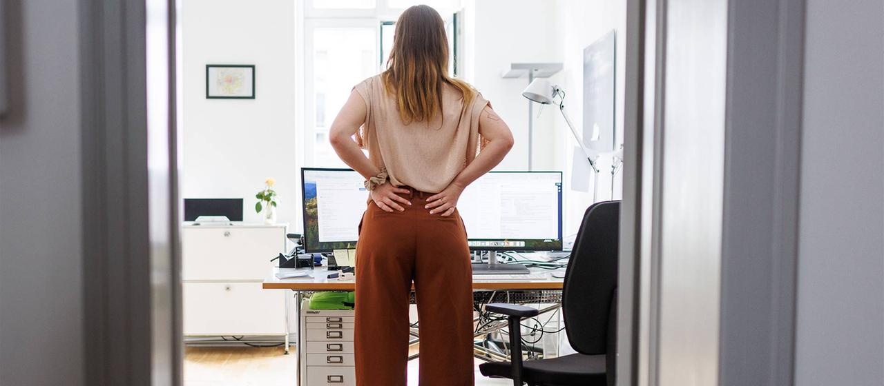 Eine Frau mit Rückenschmerzen steht in einem Büro.