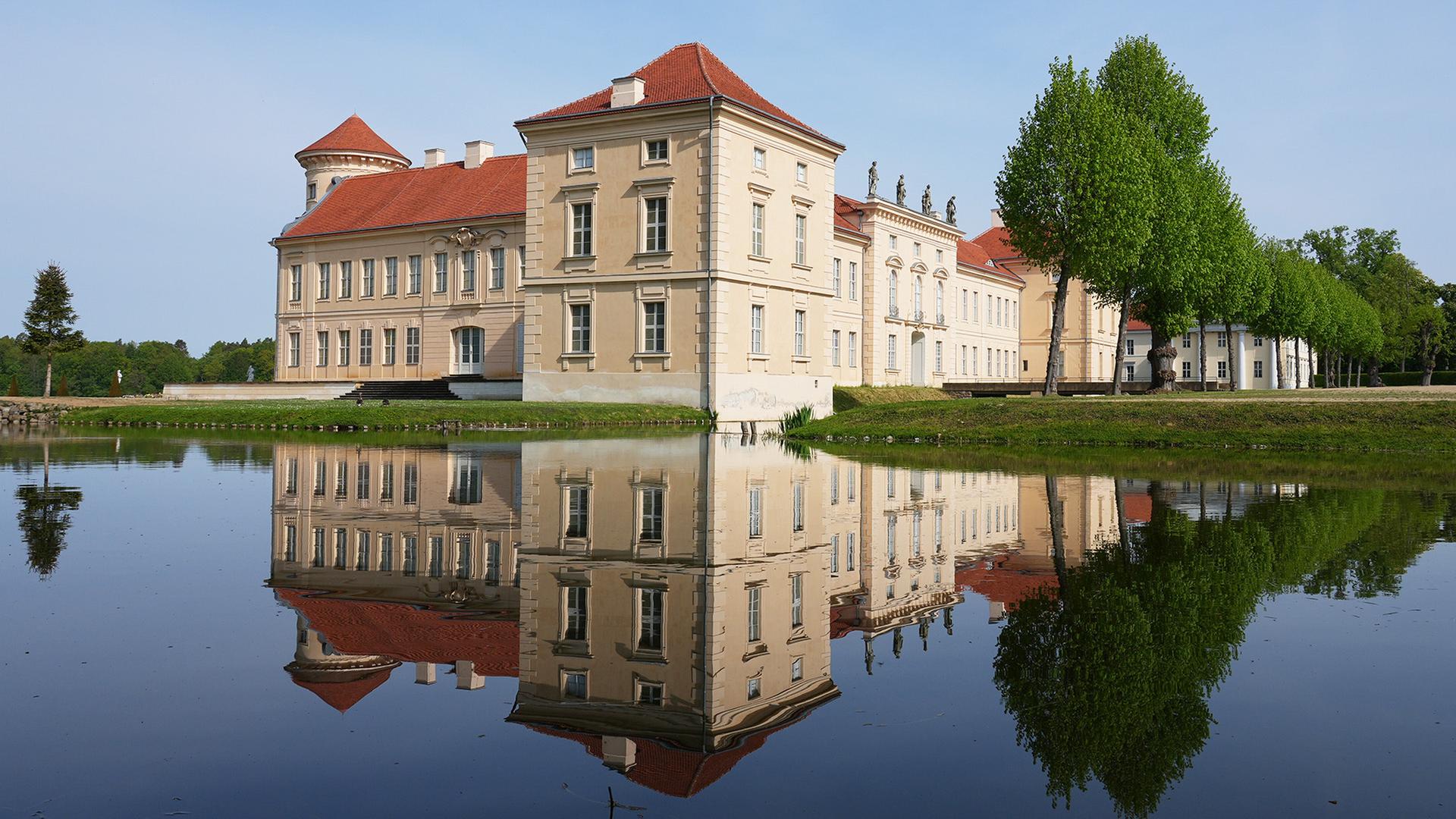 Die Parkseite von Schloss Rheinsberg mit dem Kurt Tucholsky Literaturmuseum spiegelt sich in dem vom Grienericksee. (Quelle: dpa/Stache) | dpa/Stache