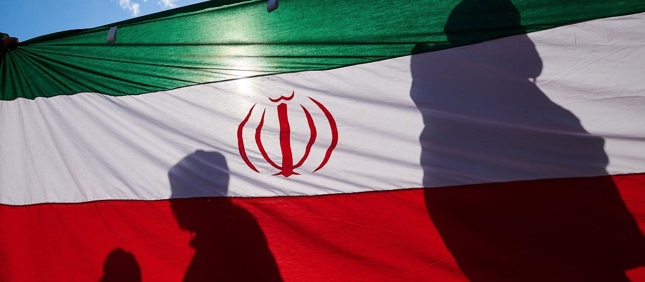 Menschen werfen Schatten auf eine iranische Flagge.