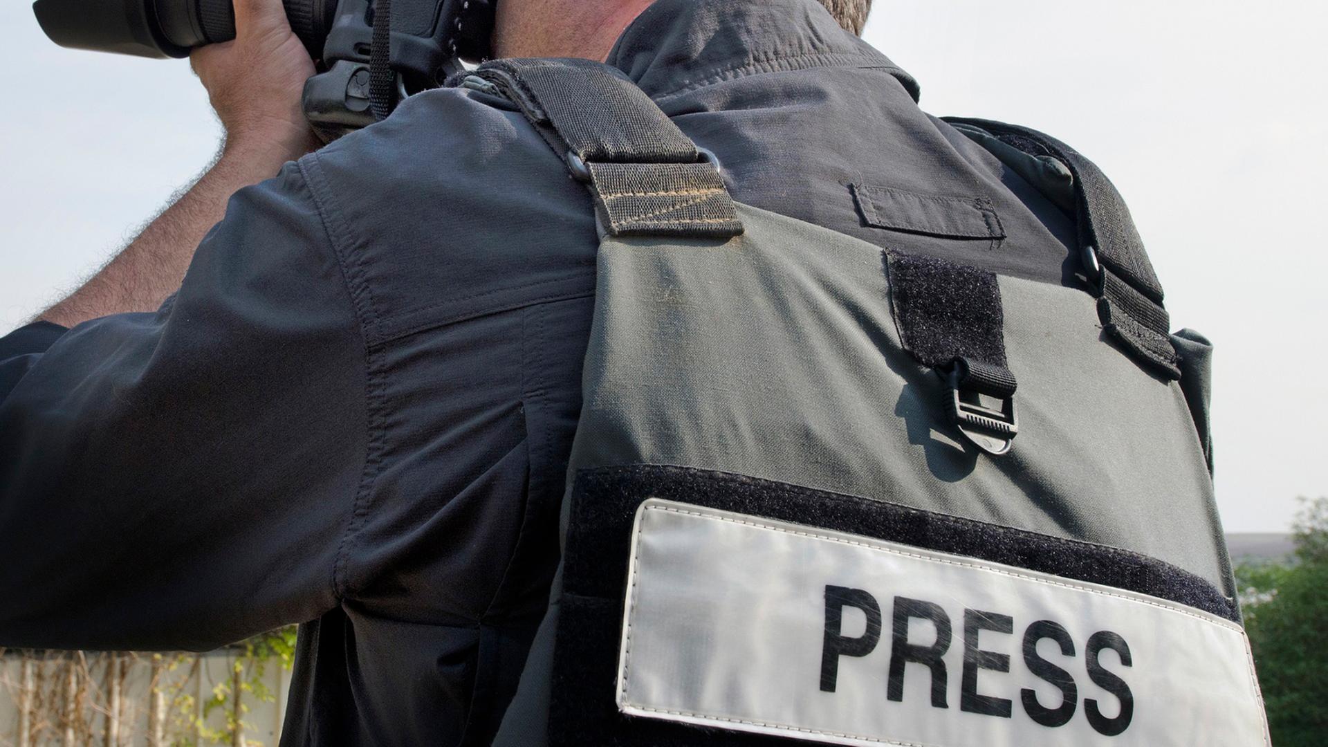 Ein Mann trägt eine Weste mit der Aufschrift Press und hält eine Kamera mit Teleobjektiv | picture alliance / Photoshot