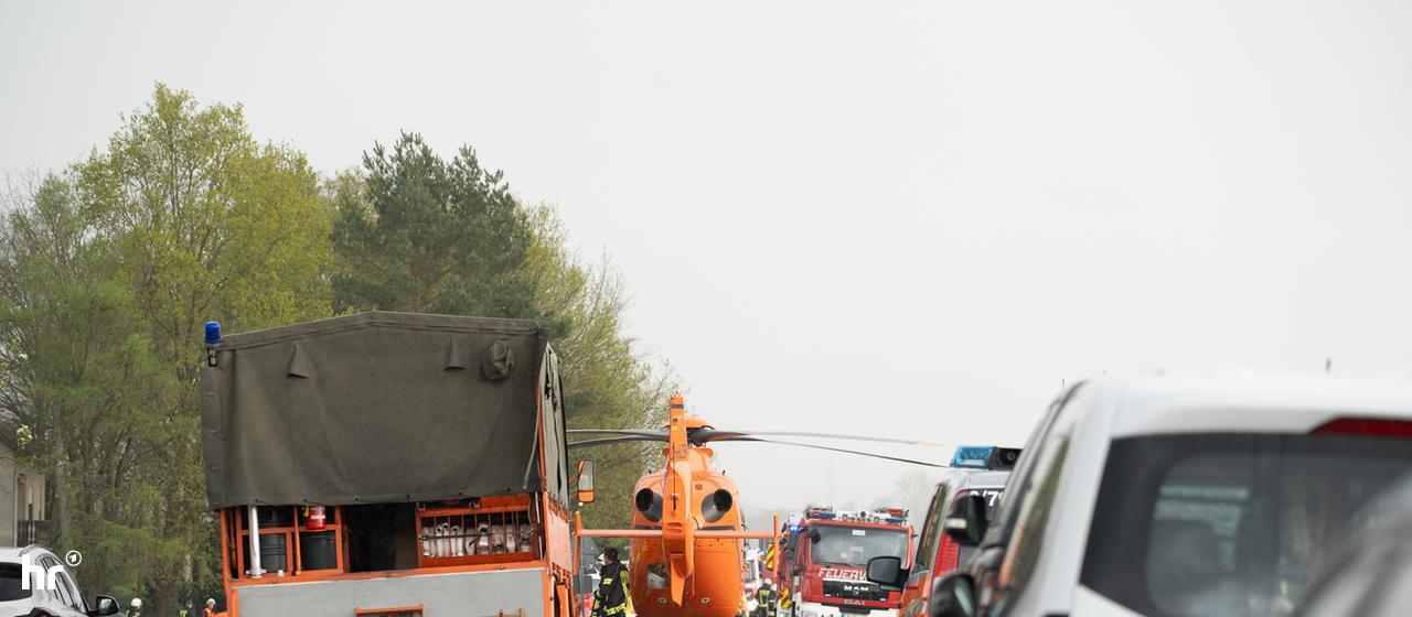 Einsatzfahrzeuge und ein Rettungshubschrauber stehen auf einer Landstraße.