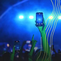 Eine Frau hält ihr Handy bei einem Konzert auf die Bühne.