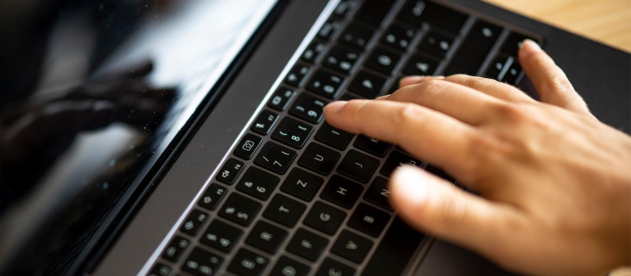 Eine Hand tippt auf der Tastatur eines Laptops.