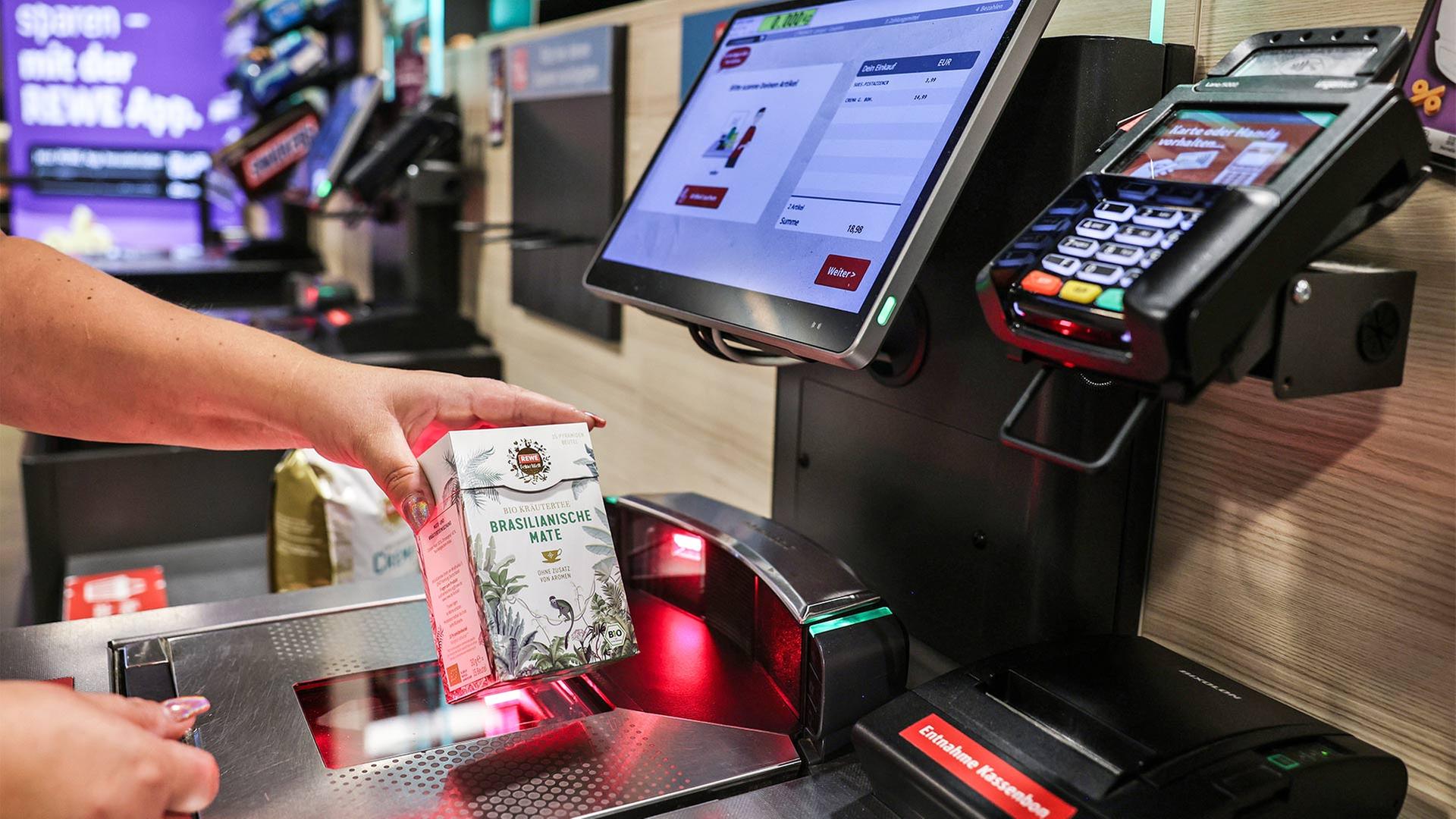 Eine Frau scannt in einem Supermarkt ein Produkt an einer Selbstbedienungskasse. | picture alliance/dpa