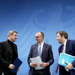 Friedrich Merz steht zwischen Lars Klingbeil und Markus Söder. Alle lächeln und halten Papiere in der Hand.