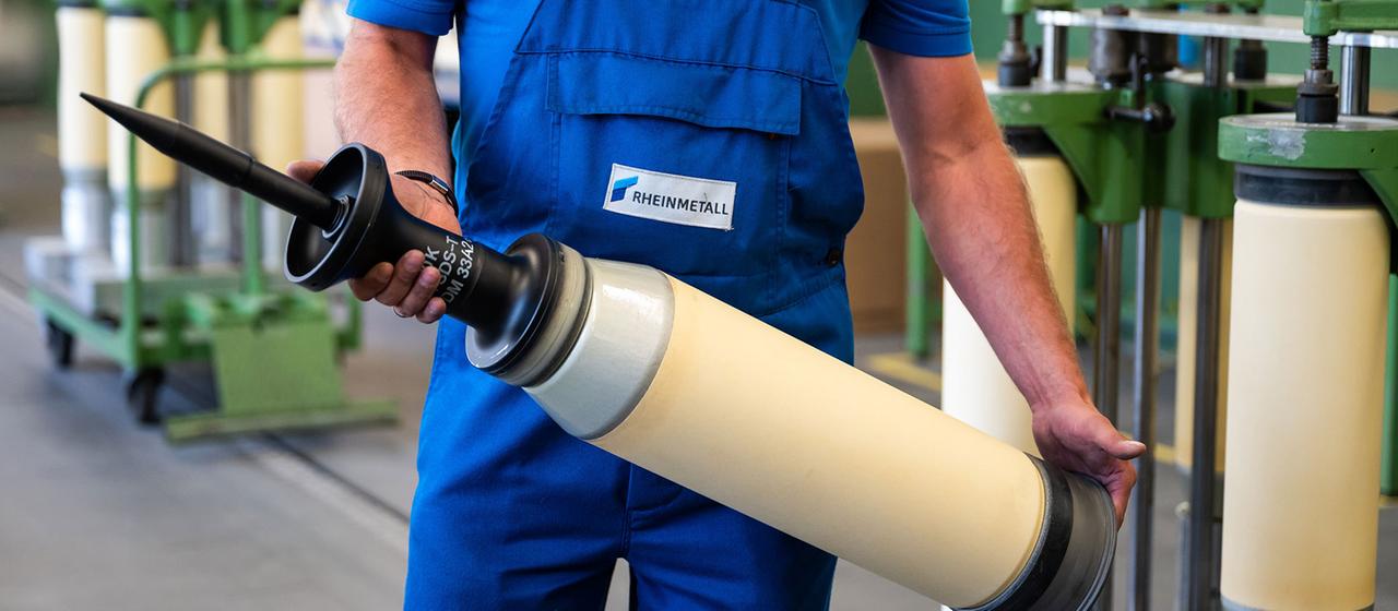 Ein Rheinmetall Mitarbeiter hält ein Panzergschoss in den Händen.