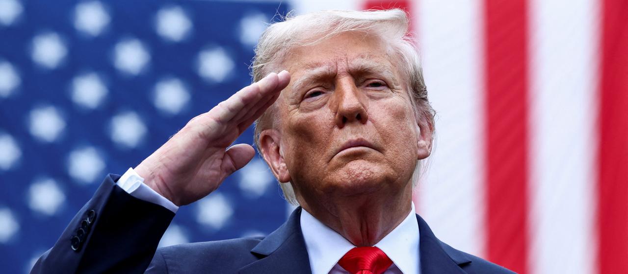 Trump salutiert vor einer US-Flagge.