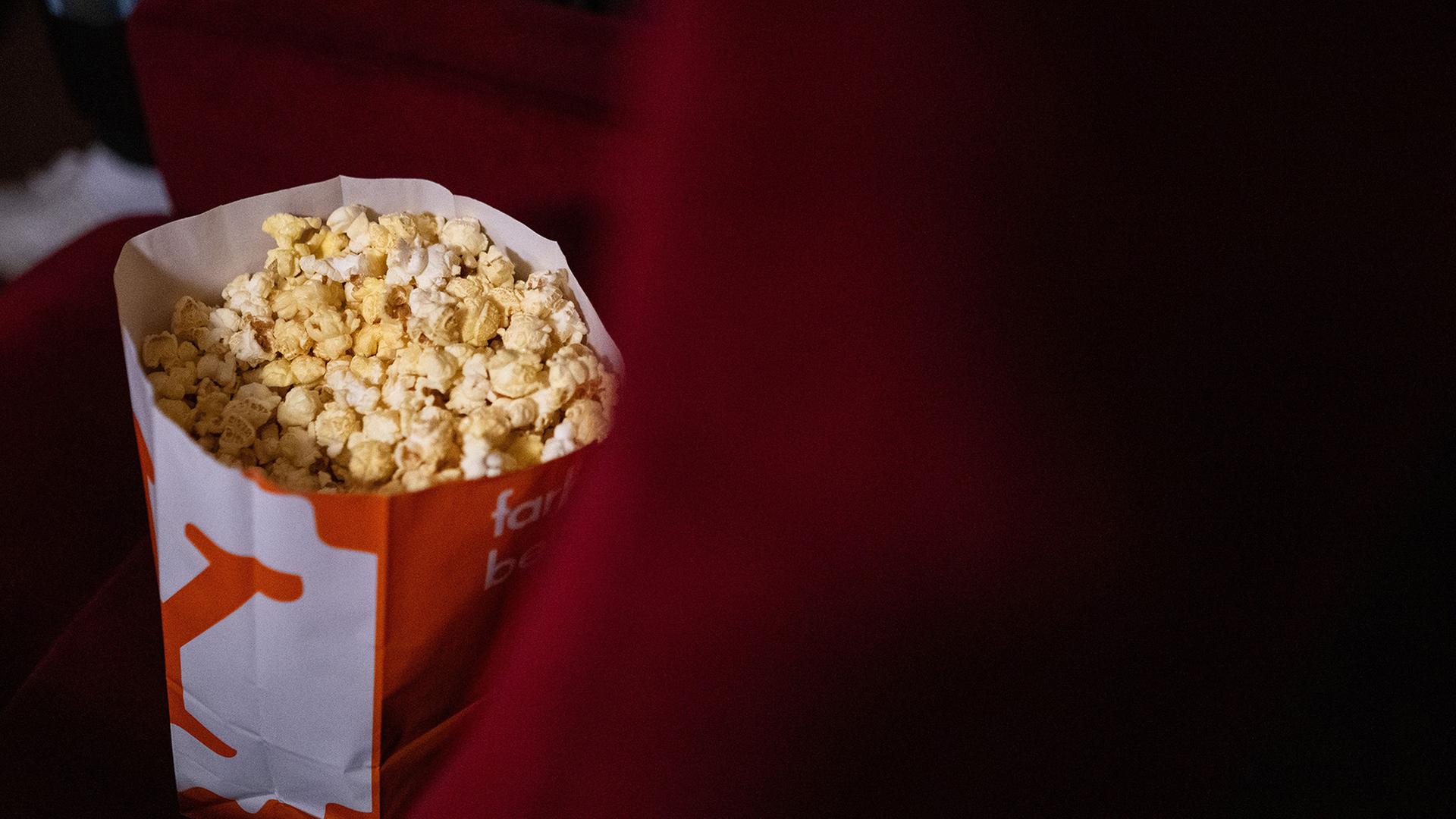 Eine Tüte mit Popcorn steht während einer Vorführung in einem Kino. | Sebastian Gollnow/dpa