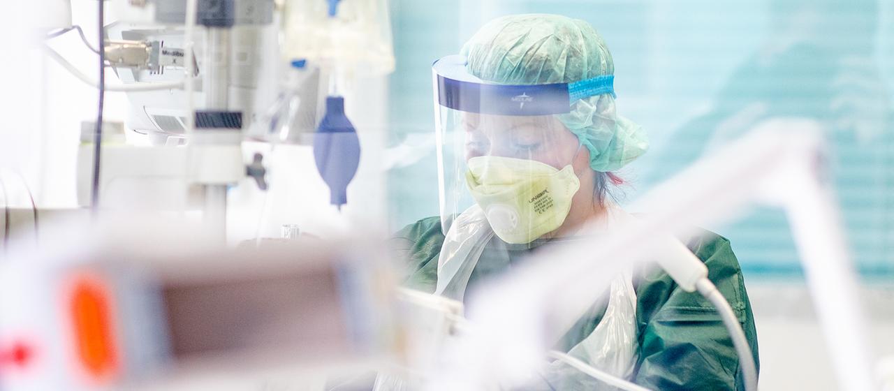 Eine Krankenpflegerin arbeitet in in Schutzkleidung in einem Krankenzimmer auf der Intensivstation des Uniklinikums Essen