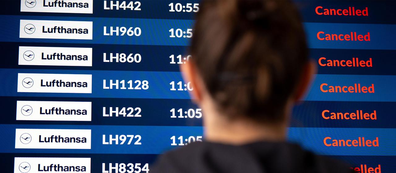 Ein Flugast vor einer Anzeigetafel für Abflüge an einem Flughafen.