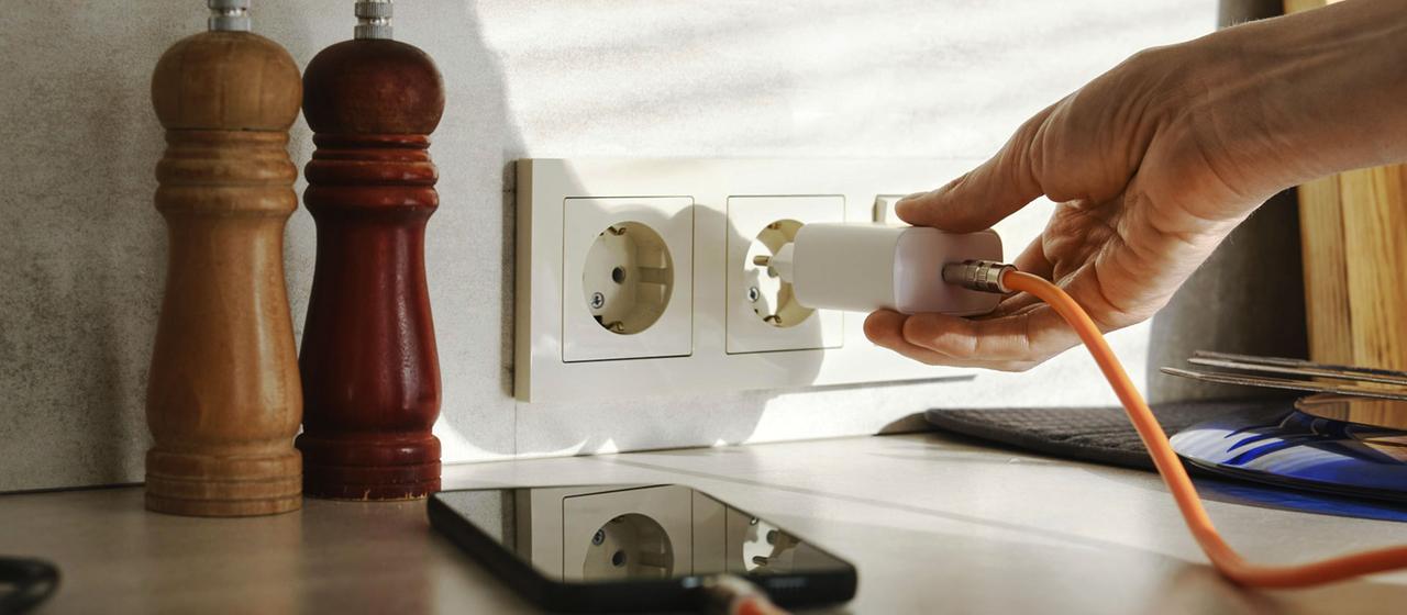 Eine Person schließt ein Smartphone Ladegerät an eine Steckdose an