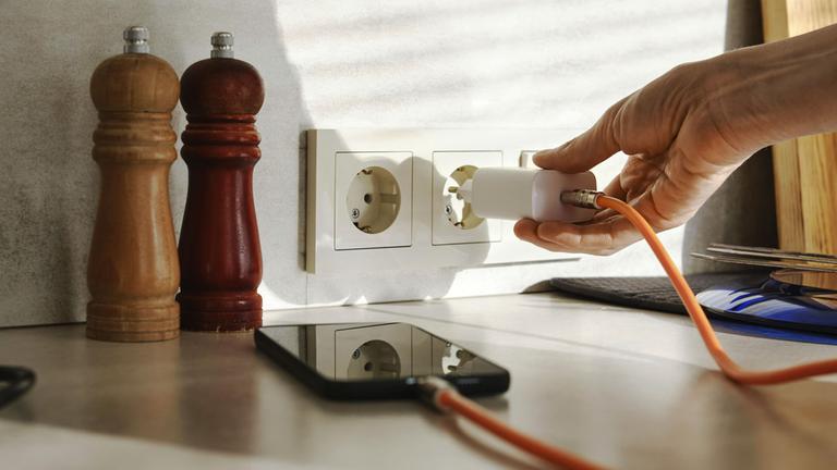 Eine Person schließt ein Smartphone Ladegerät an eine Steckdose an
