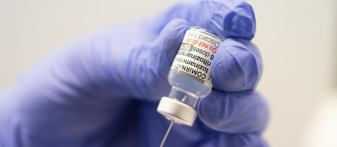 Eine Hand zieht eine Spritze mit dem Corona-Impfstoff von BioNTech auf