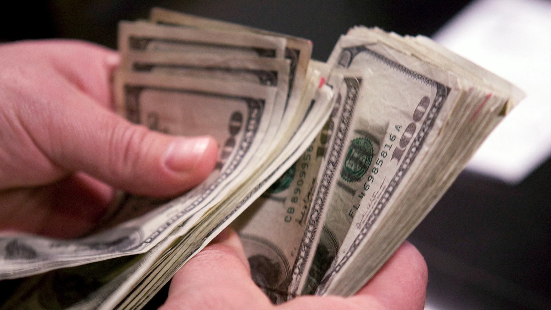 Hände halten ein Bündel mit Dollar-Geldscheinen. | REUTERS