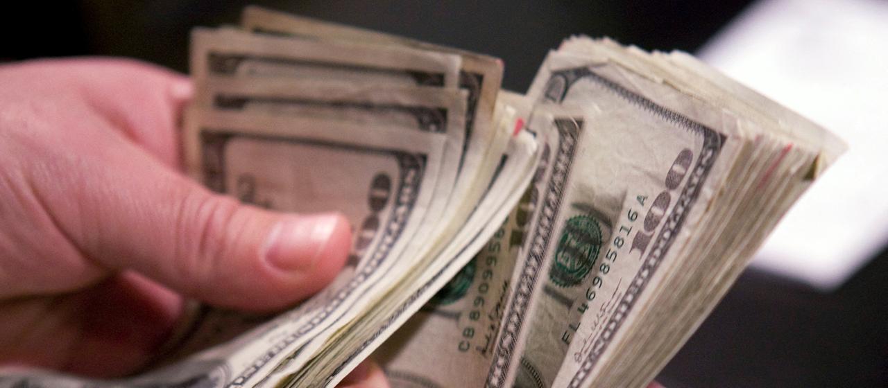Hände halten ein Bündel mit Dollar-Geldscheinen.