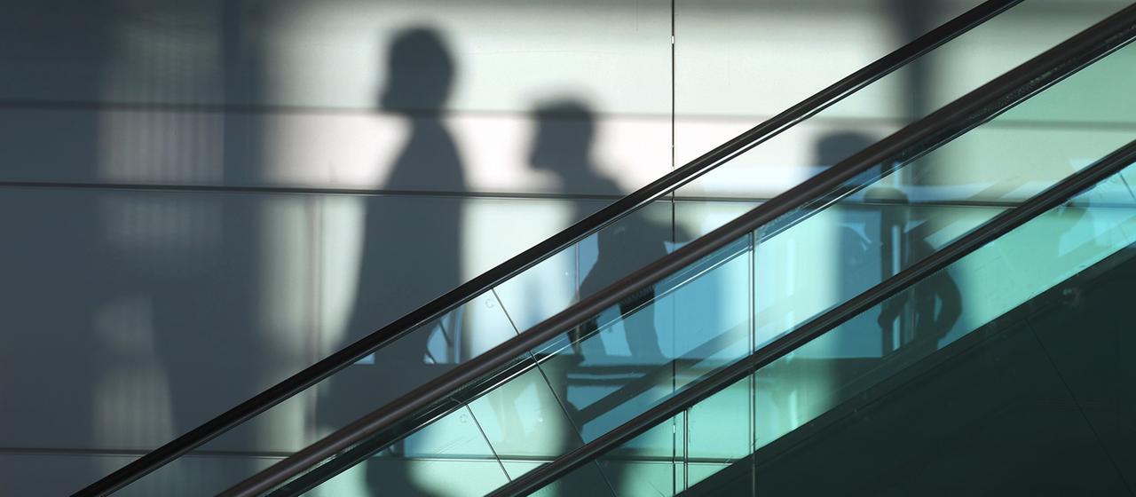 Schatten von Menschen hinter einer Rolltreppe
