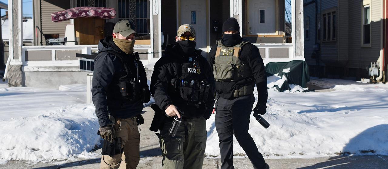 ICE-Einsatzkräfte mit Gesichtsmasken stehen vor einem Haus in Minneapolis (Minnesota).