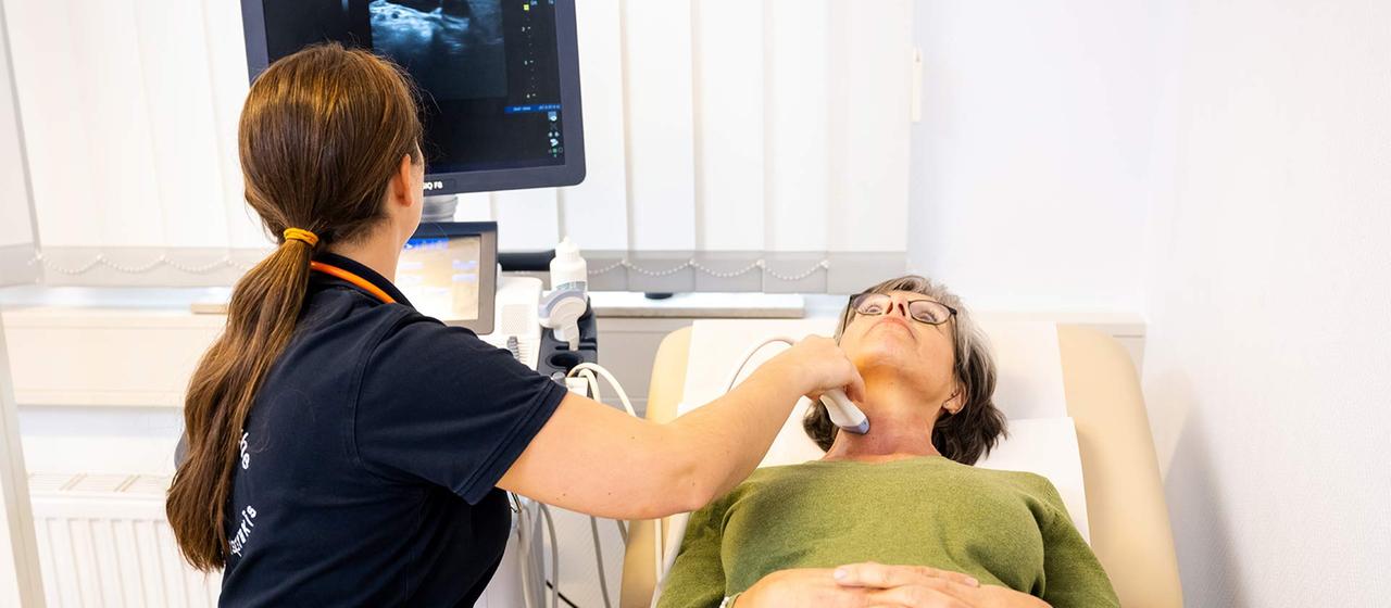 Eine Hausaerztin führt eine Ultraschalluntersuchung bei einer Patientin durch.