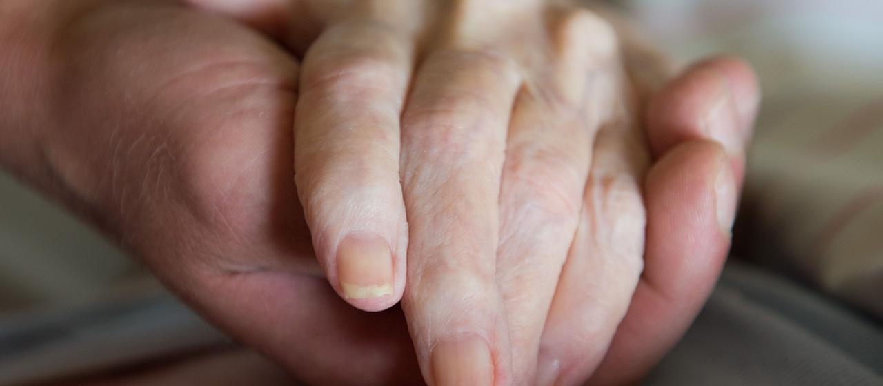 Ein Altenpfleger hält in einem Pflegeheim die Hand einer Frau.