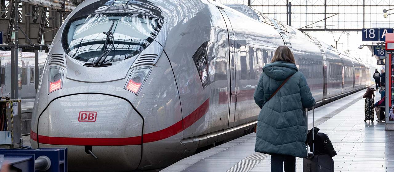 Eine Reisende mit Rollkoffer geht auf einem Bahnsteig an einem ICE vorbei.
