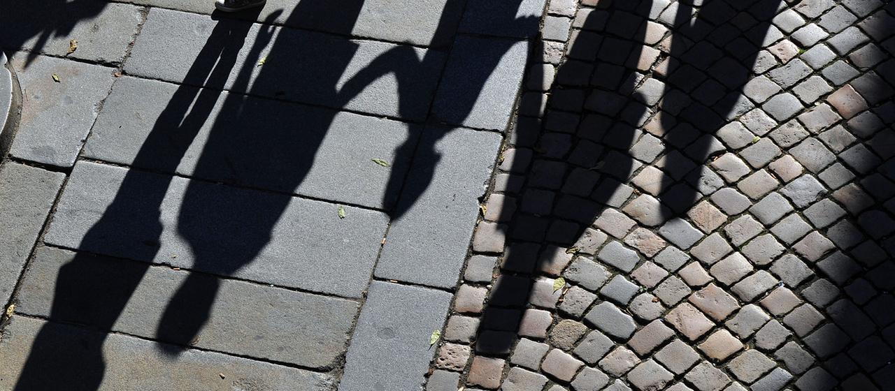 Schatten von Menschen verschiedenen Alters auf Kofpsteinpflaster.