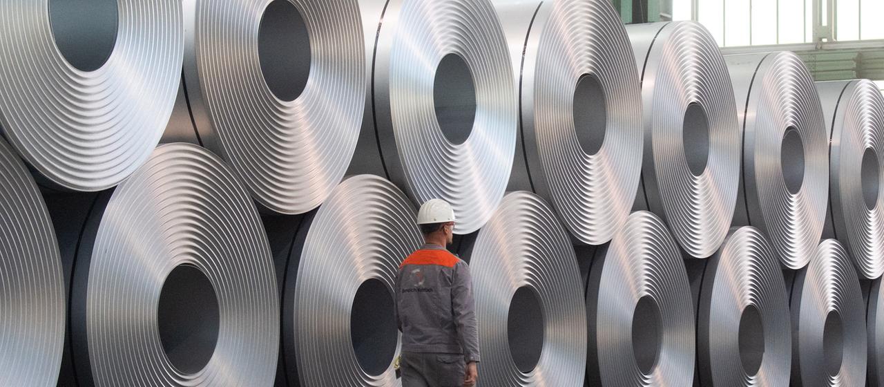 Eine Mitarbeiter geht bei der Salzgitter AG an aufgewickeltem Stahl (Coils) vorbei