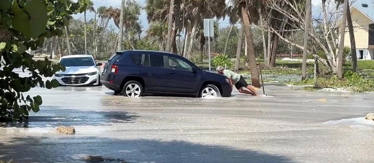 Ein Mann schiebt ein Auto auf einer von Regen überfluteten Straße.