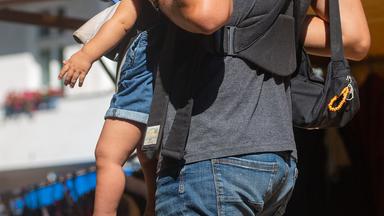 Ein Mann trägt ein Kleinkind in einer Tragehilfe durch eine Fußgängerzone.