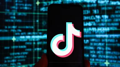 Das Logo der Video-App TikTok auf  einem Smartphone vor Bildschirmen.