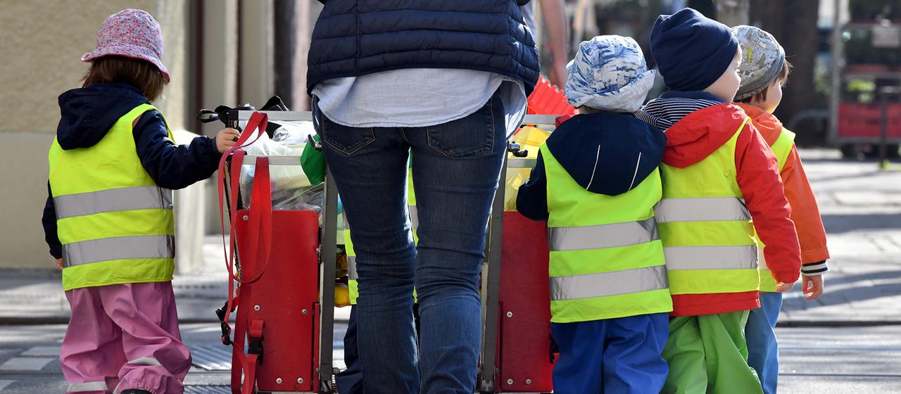 Ein Betreuerin läuft mit mehreren Kleinkindern über einen Bürgersteig.