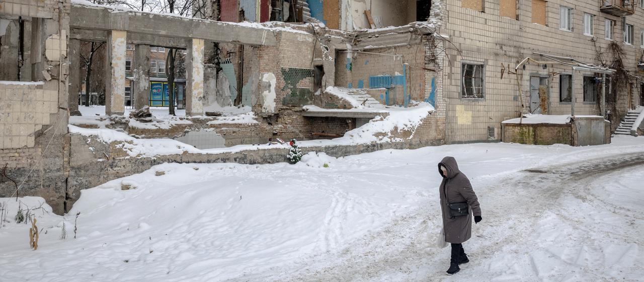 Eine Frau läuft in Kiew (Ukraine) an einem zerstörten Gebäude vorbei durch den Schnee.