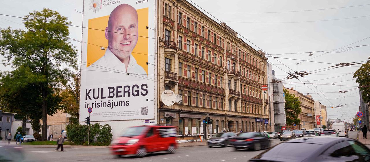An einer Hauswand hängt ein Wahlplakat von Andris Kulbergs.